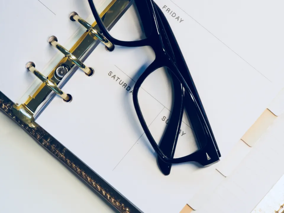 A pair of dark glasses resting on an open ring-bound weekly planner showing Friday, Saturday and Sunday