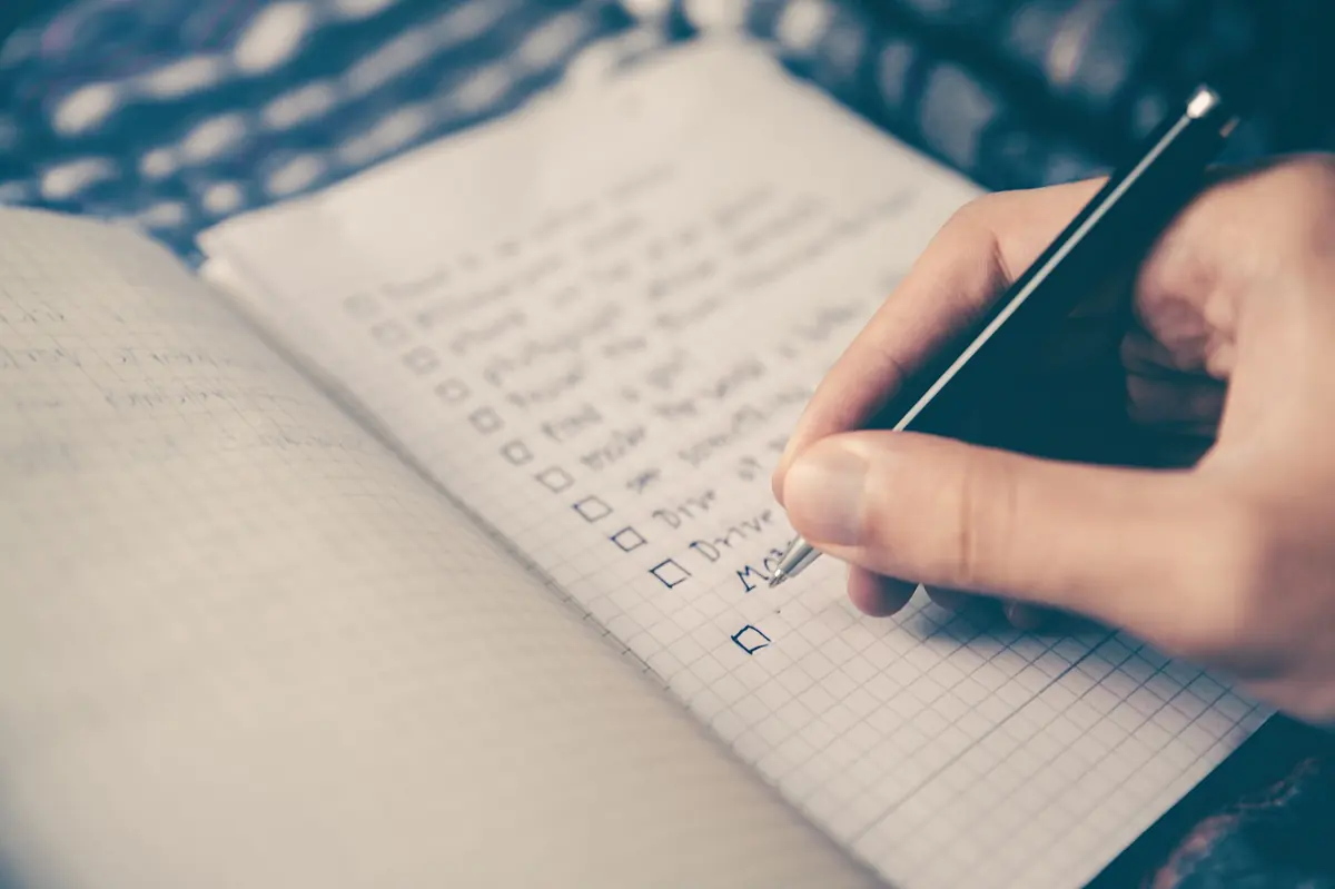 A hand with a pen working down a row of tick boxes on a paper checklist