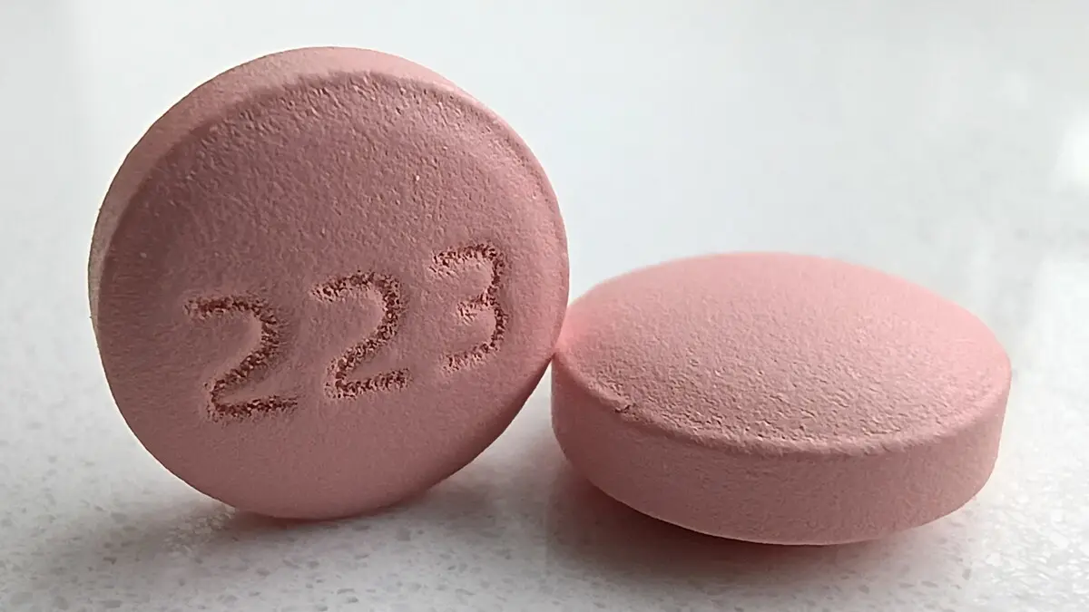 Two pink round tablets on a white surface, one standing on its edge with the number 223 pressed into it, labeled by the photographer as lithium carbonate extended-release 300 mg