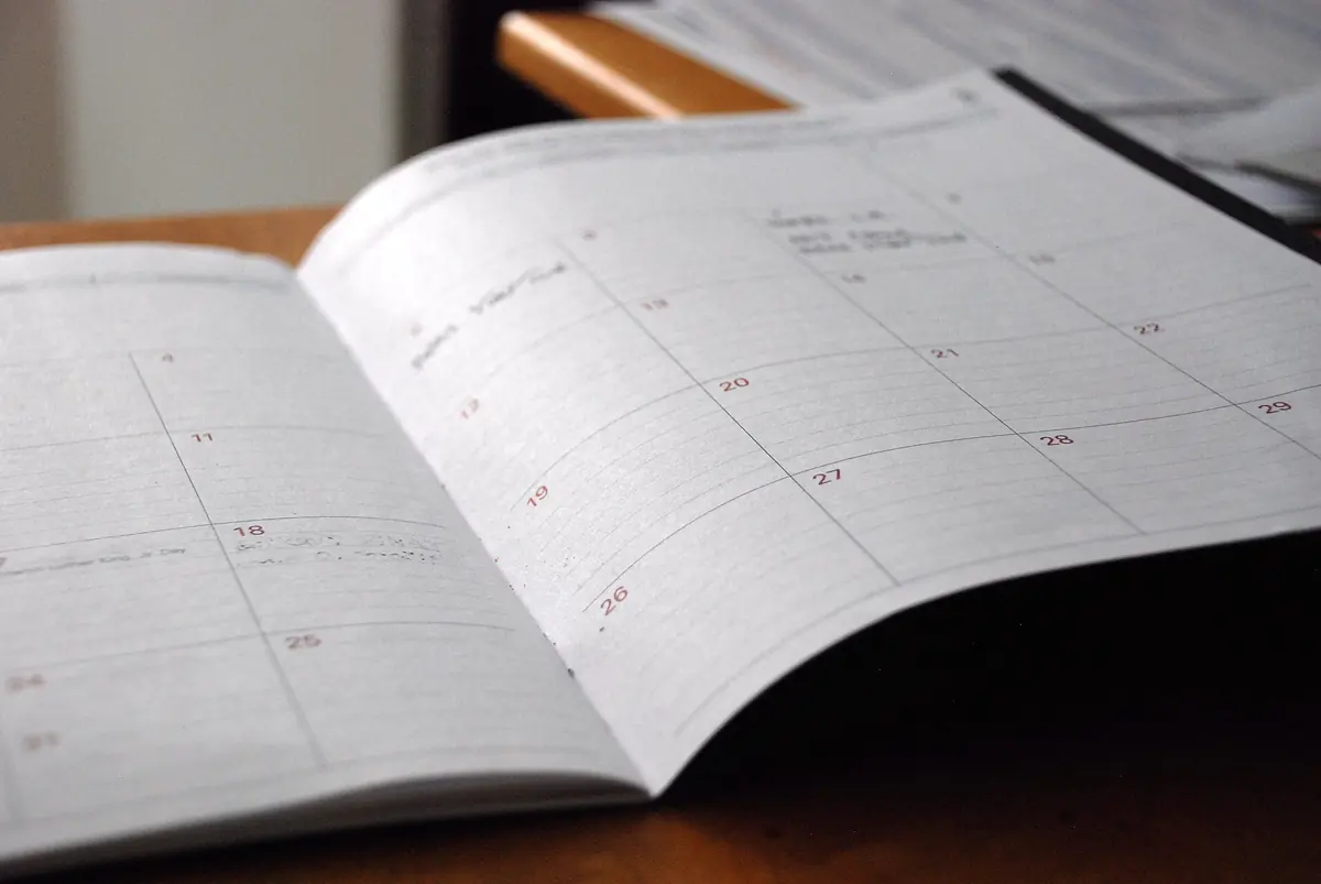 An open month-view paper planner lying on a wooden desk