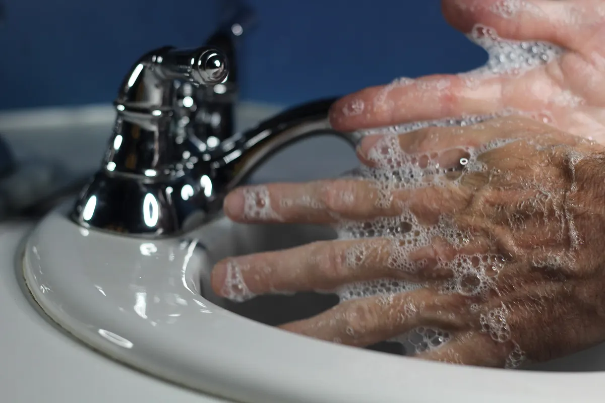 Close-up of soapy hands rubbing together under a chrome tap over a white sink