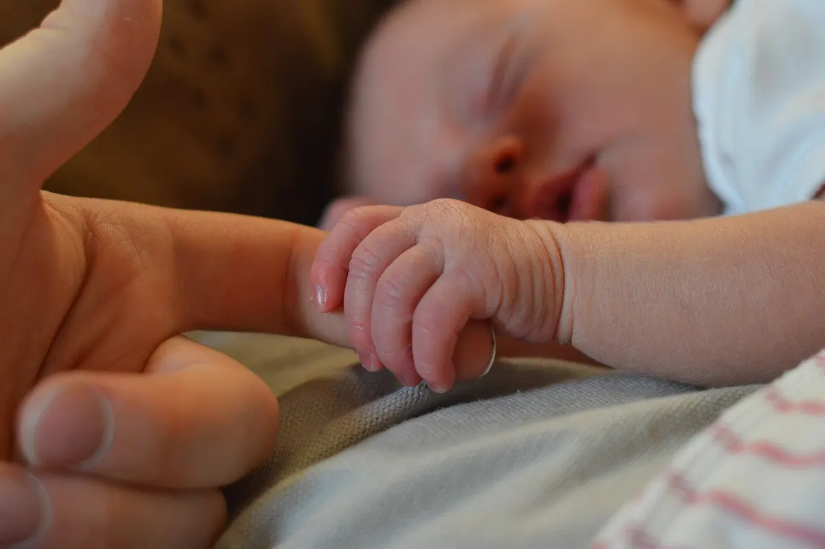 A sleeping newborn’s hand holding an adult’s finger
