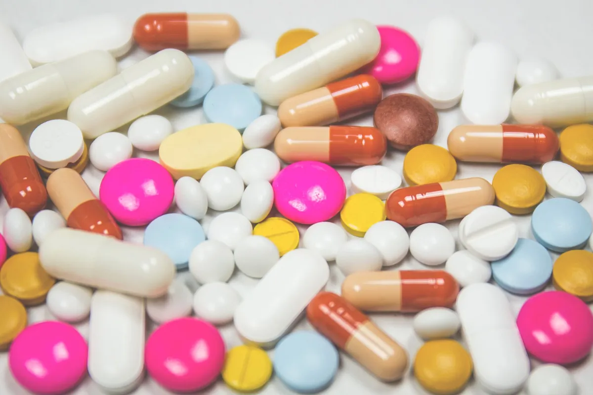 A pile of white, yellow, pink, blue and orange-and-white tablets and capsules on a white surface