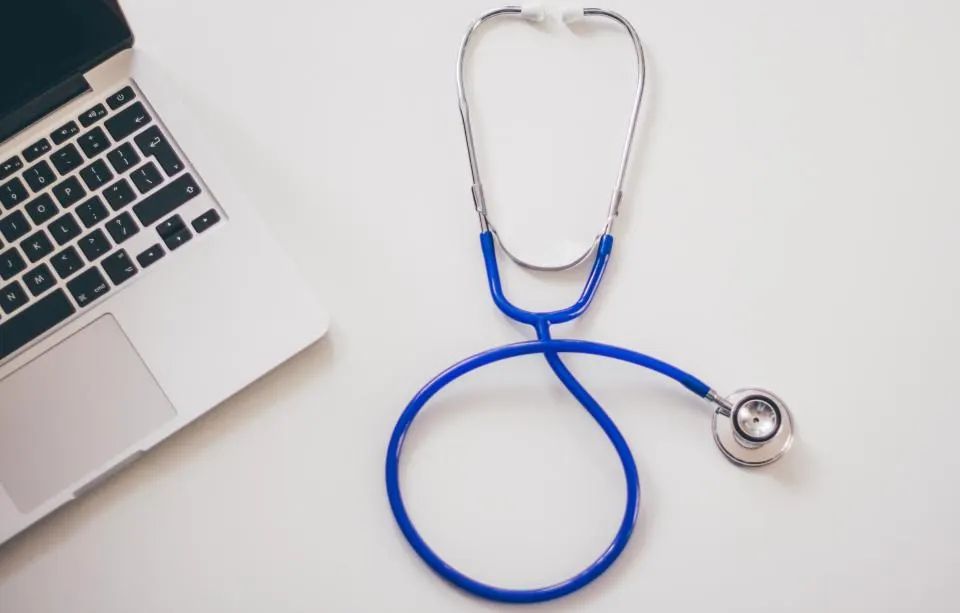 A blue stethoscope on a white desk next to an open laptop