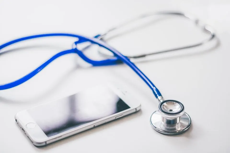 A smartphone lying on a white table beside a blue stethoscope