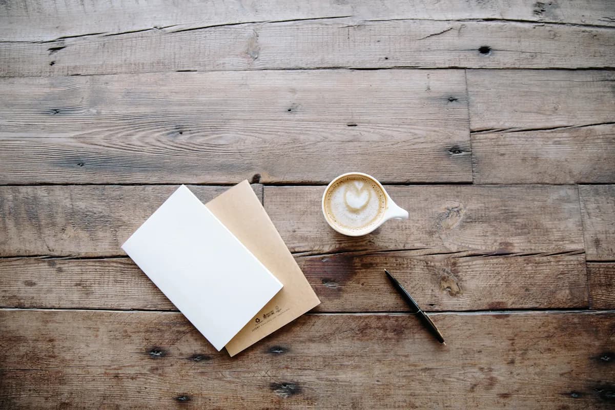 Two notebooks, a pen and a cup of coffee on a wooden table