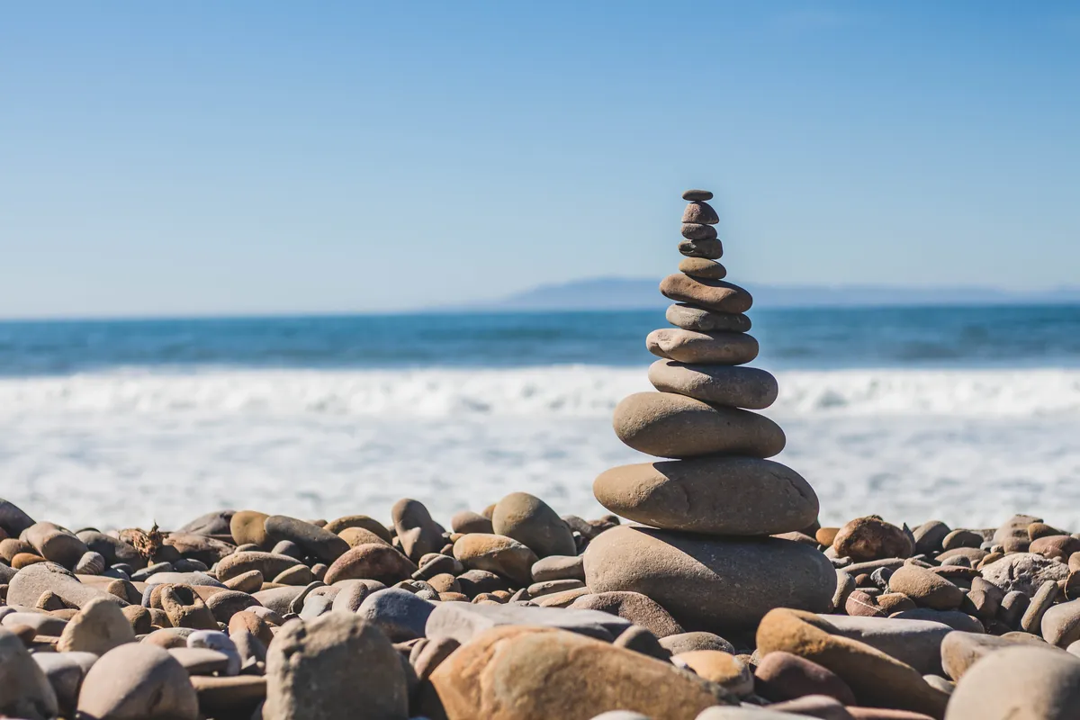 A tower of smooth stones balanced on a pebble beach, with the sea behind