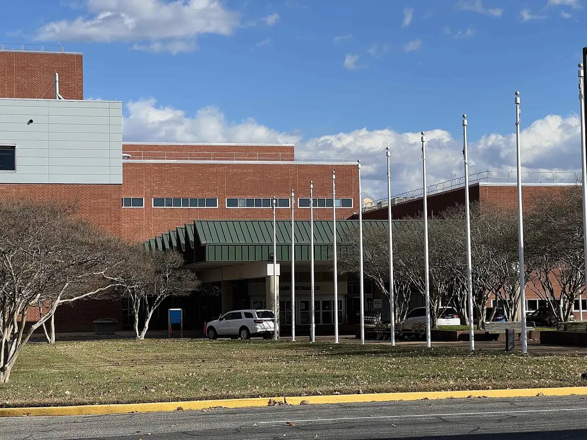 The main entrance of a red-brick VA medical center under a blue sky, with a green canopy, a row of flagpoles and bare trees on the lawn